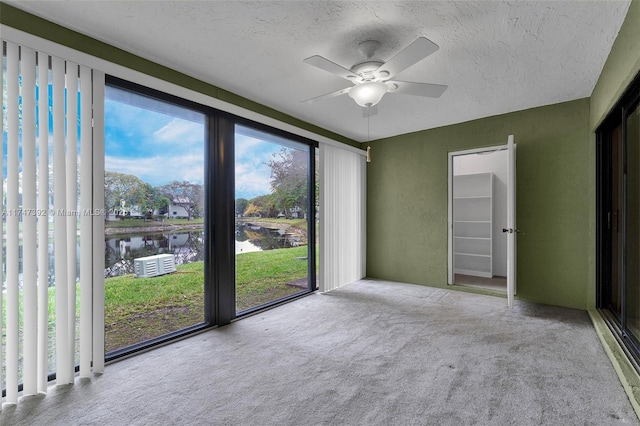 unfurnished room featuring a water view, ceiling fan, a textured ceiling, and light colored carpet