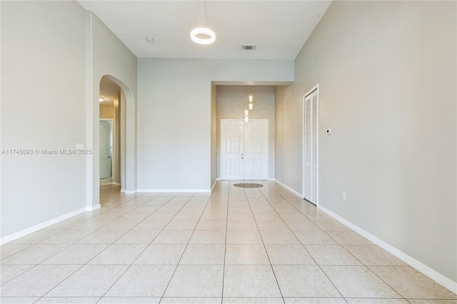 unfurnished room featuring arched walkways, light tile patterned flooring, visible vents, and baseboards