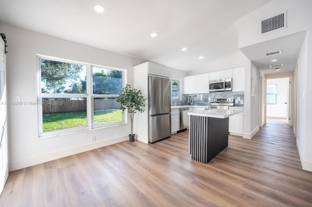 kitchen with a barn door, stainless steel appliances, a kitchen island, white cabinetry, and light countertops