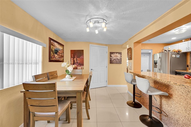 dining space featuring light tile patterned floors, a textured ceiling, and baseboards