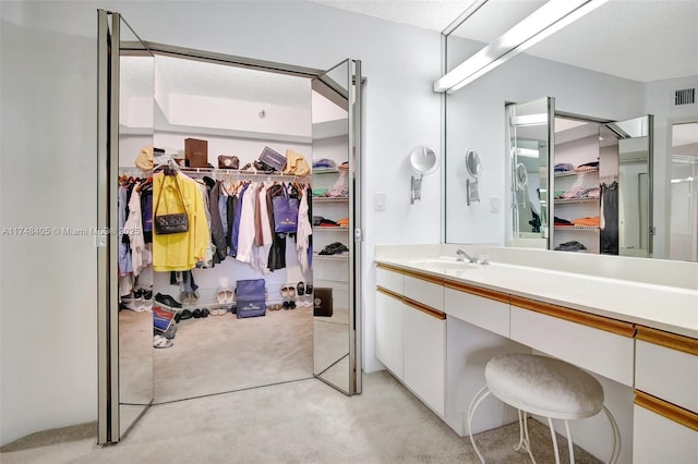 bathroom featuring a textured ceiling, visible vents, a walk in closet, and vanity
