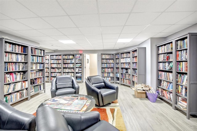 sitting room featuring bookshelves, a drop ceiling, and wood finished floors