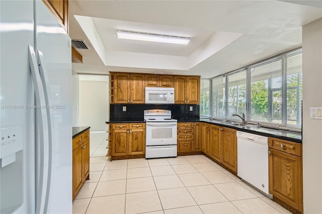 kitchen with brown cabinets, a raised ceiling, visible vents, backsplash, and white appliances