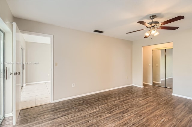 spare room with a ceiling fan, dark wood-style flooring, visible vents, and baseboards