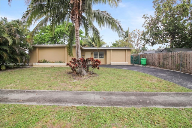 view of front facade with driveway, a front yard, fence, and stucco siding