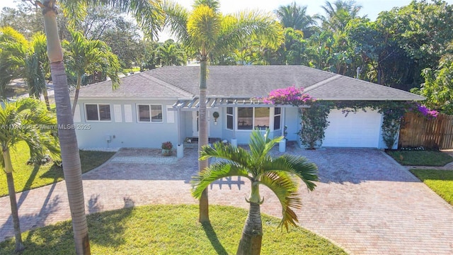 single story home featuring a shingled roof, an attached garage, decorative driveway, a front lawn, and stucco siding