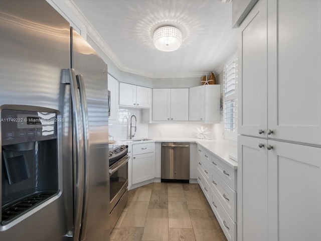 kitchen featuring white cabinets, appliances with stainless steel finishes, light countertops, crown molding, and a sink