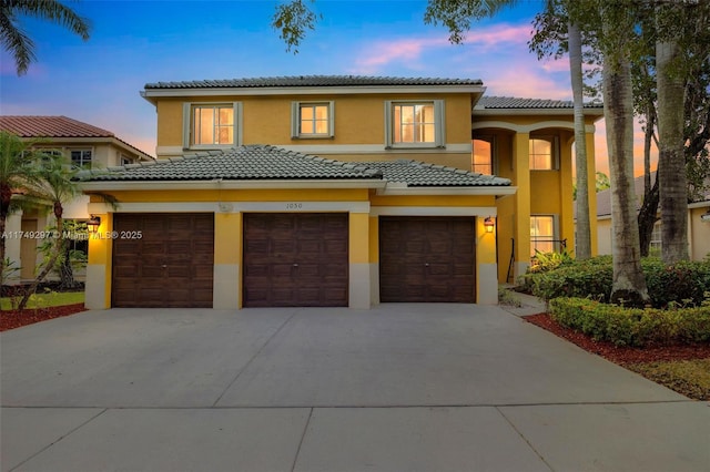 mediterranean / spanish-style home with a garage, a tile roof, concrete driveway, and stucco siding