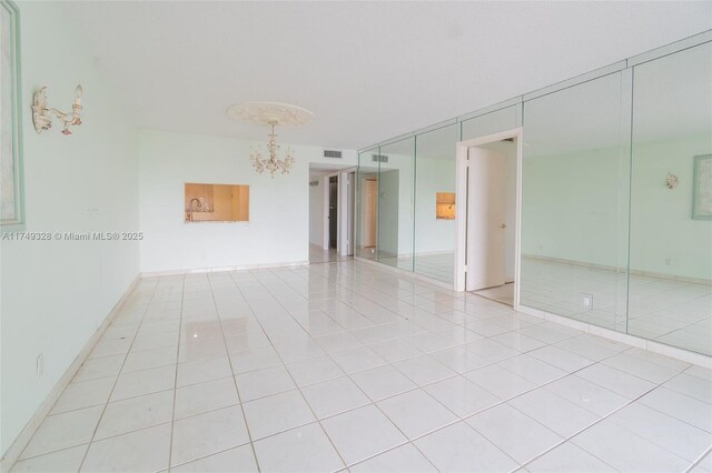 empty room with an inviting chandelier, baseboards, visible vents, and light tile patterned flooring