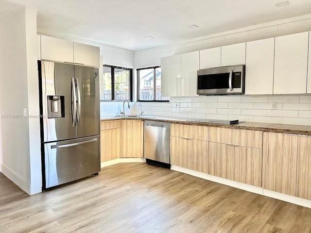 kitchen featuring appliances with stainless steel finishes, a sink, light wood-style flooring, and decorative backsplash