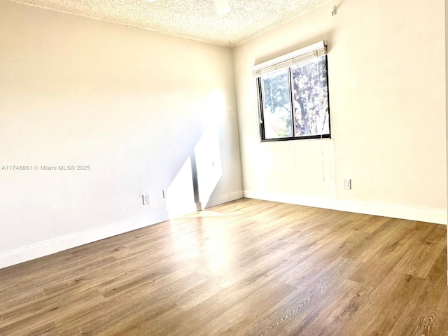 empty room featuring a textured ceiling, wood finished floors, and baseboards