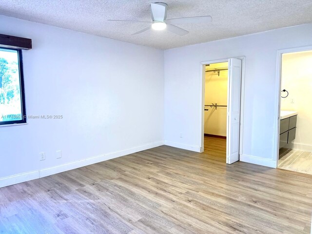 unfurnished bedroom with wood finished floors, a textured ceiling, a walk in closet, a closet, and baseboards