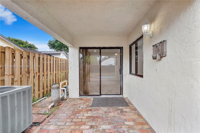 view of exterior entry with central AC, stucco siding, and a patio area
