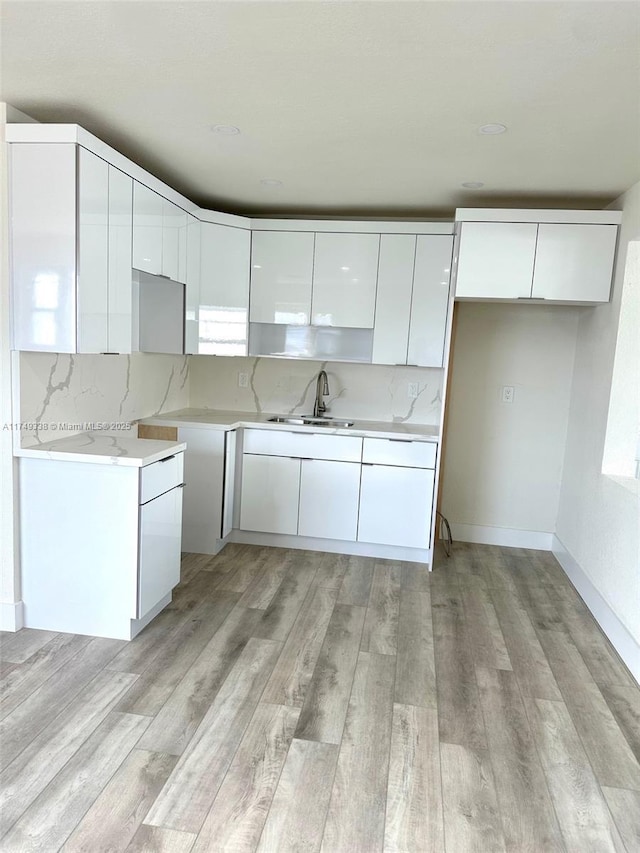 kitchen featuring white cabinets, modern cabinets, backsplash, light wood-style floors, and a sink