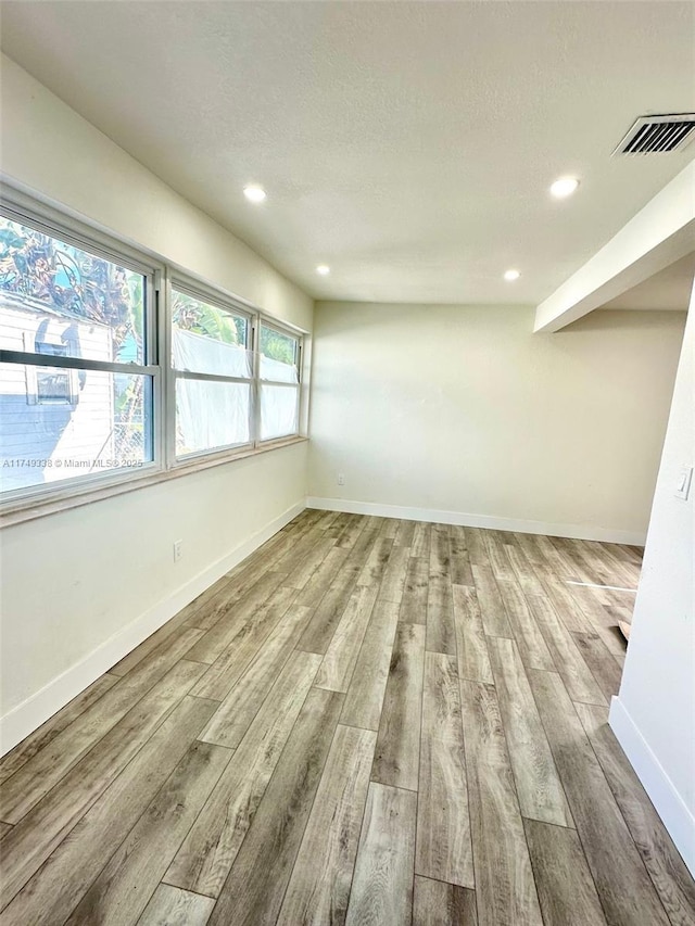 unfurnished room featuring light wood finished floors, baseboards, visible vents, and a textured ceiling