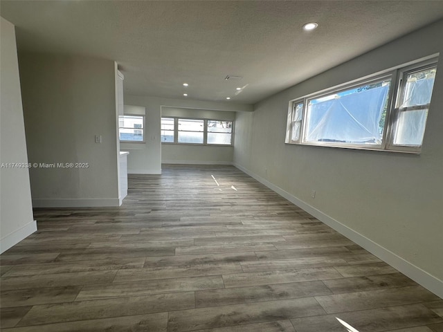 empty room featuring a textured ceiling, baseboards, and wood finished floors