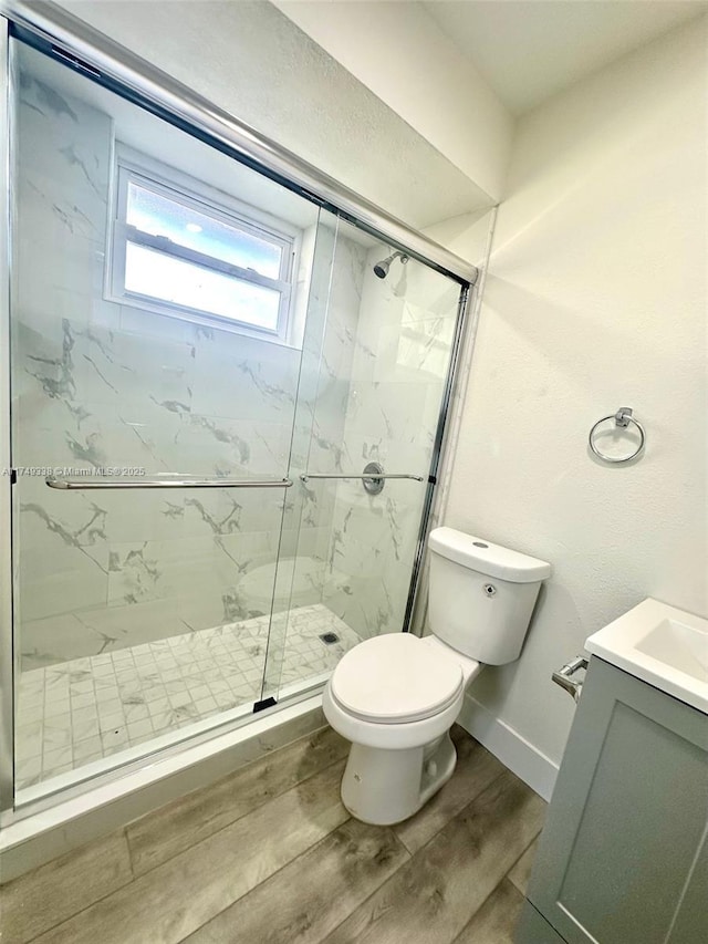 bathroom featuring a marble finish shower, toilet, vanity, wood finished floors, and baseboards