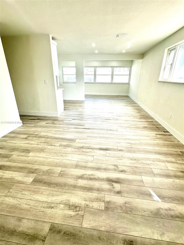 empty room featuring light wood-style flooring, baseboards, and a textured ceiling