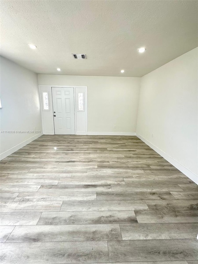 spare room with baseboards, visible vents, a textured ceiling, light wood-type flooring, and recessed lighting