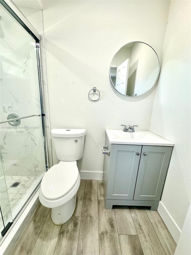 bathroom with toilet, a marble finish shower, vanity, and wood finish floors