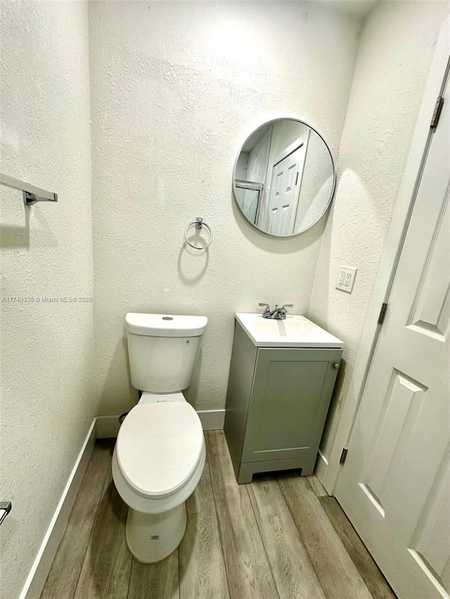 bathroom with a textured wall, toilet, vanity, wood finished floors, and baseboards