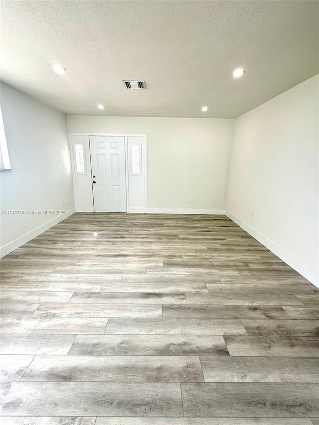 empty room with a textured ceiling, recessed lighting, visible vents, baseboards, and light wood-style floors