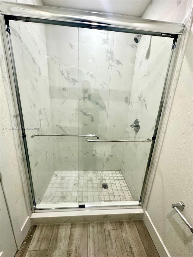 full bath with a stall shower, a textured wall, baseboards, and wood finished floors