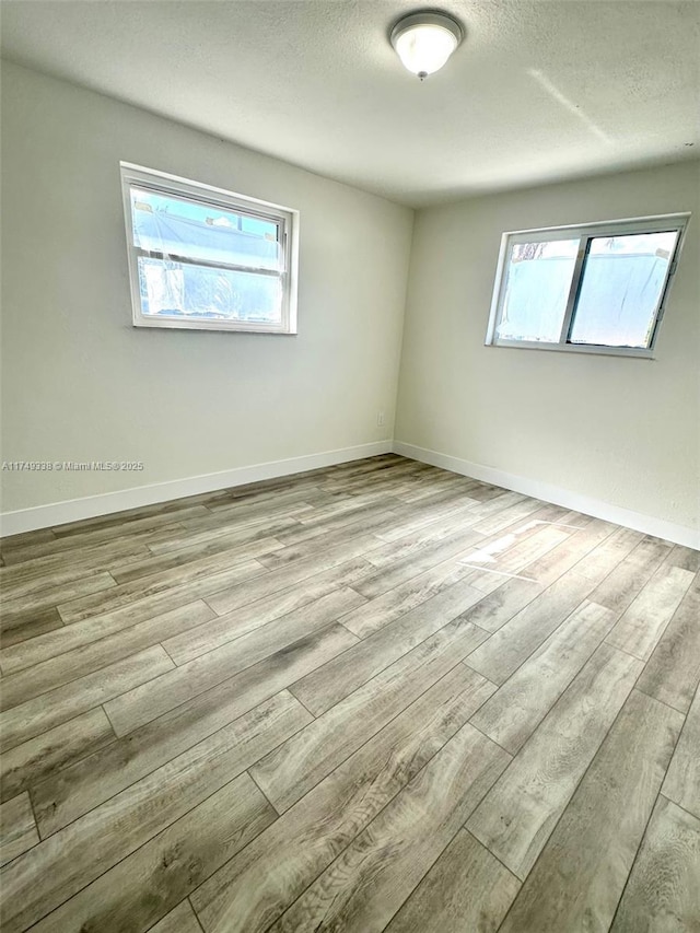 spare room featuring light wood finished floors, baseboards, and a textured ceiling