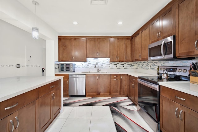 kitchen with hanging light fixtures, a sink, stainless steel appliances, light countertops, and backsplash