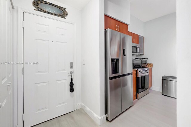 kitchen featuring appliances with stainless steel finishes, brown cabinetry, light wood-style flooring, and baseboards