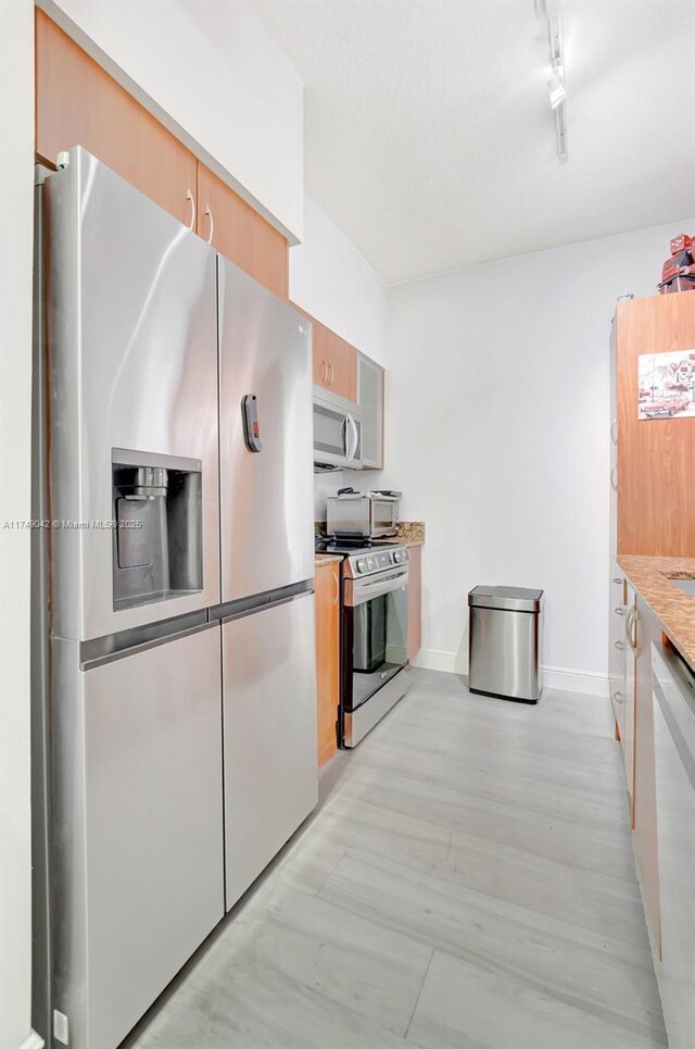 kitchen featuring rail lighting, baseboards, stainless steel appliances, and light wood-style floors