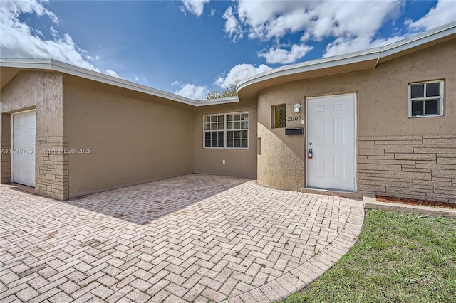 view of exterior entry with an attached garage, a patio area, and stucco siding