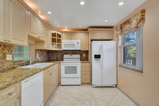 kitchen with backsplash, glass insert cabinets, a sink, light stone countertops, and white appliances