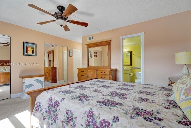 carpeted bedroom featuring multiple closets, visible vents, a ceiling fan, connected bathroom, and a textured ceiling