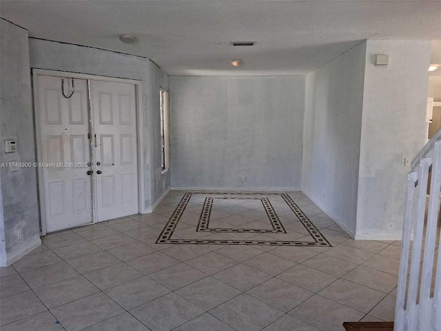 interior space featuring a textured ceiling, light tile patterned floors, and baseboards