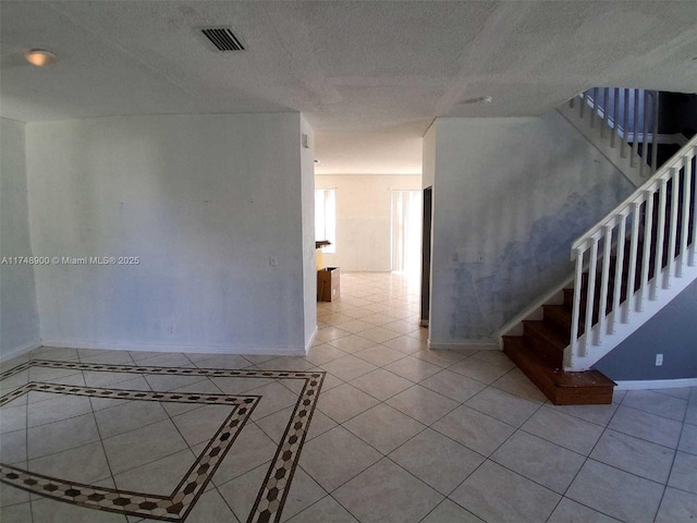 empty room with visible vents, a textured ceiling, tile patterned flooring, baseboards, and stairs