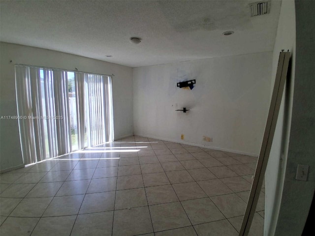 spare room featuring light tile patterned floors, baseboards, visible vents, and a textured ceiling