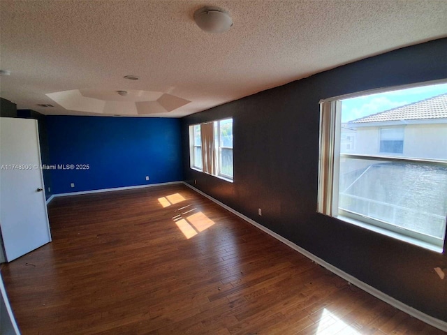 empty room featuring a raised ceiling, dark wood finished floors, a textured ceiling, and baseboards