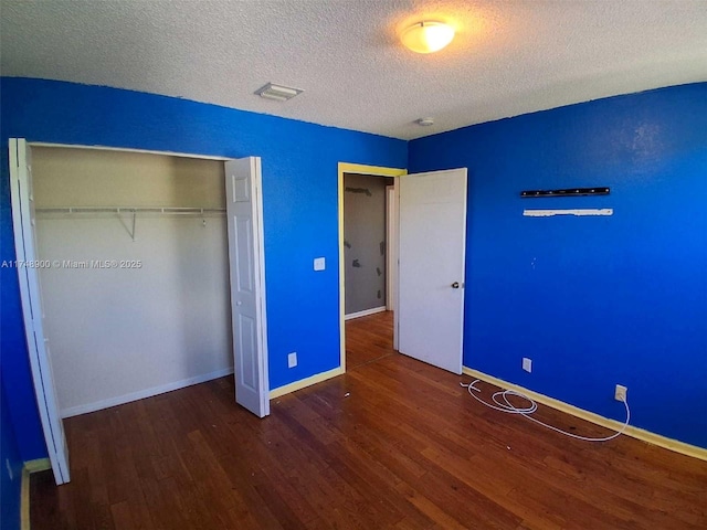 unfurnished bedroom featuring a closet, dark wood finished floors, a textured ceiling, and baseboards