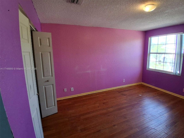 empty room featuring visible vents, baseboards, a textured wall, dark wood-style flooring, and a textured ceiling