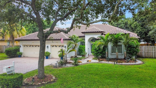 mediterranean / spanish-style home featuring a garage, a tile roof, fence, decorative driveway, and a front lawn