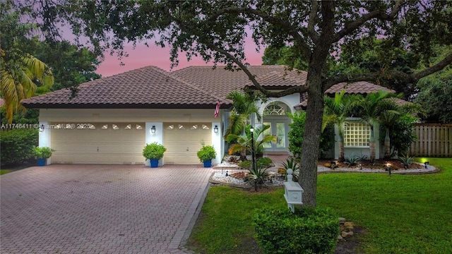 mediterranean / spanish house featuring decorative driveway, french doors, a yard, stucco siding, and a tiled roof