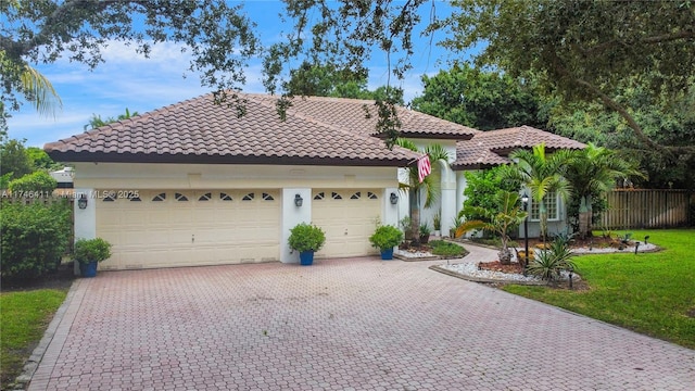 view of front of home featuring a tiled roof, an attached garage, fence, decorative driveway, and stucco siding