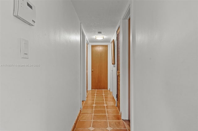 corridor featuring light tile patterned flooring, a textured ceiling, and a wall mounted AC