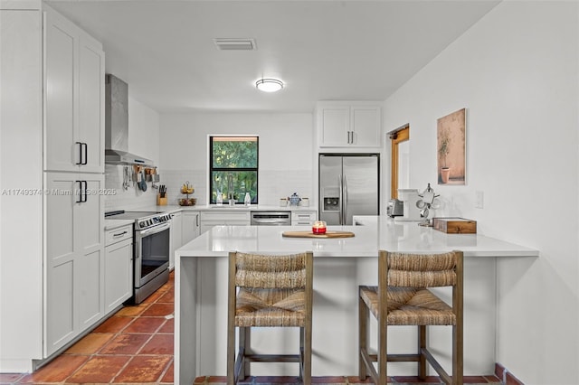 kitchen with a breakfast bar, wall chimney range hood, visible vents, and stainless steel appliances