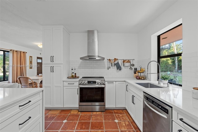 kitchen featuring tasteful backsplash, light countertops, appliances with stainless steel finishes, a sink, and wall chimney range hood