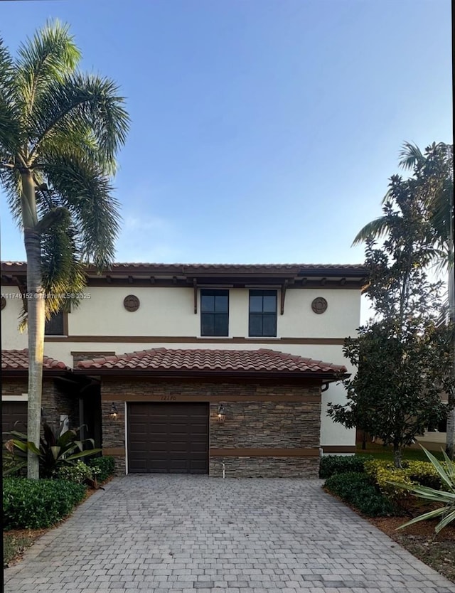 view of front facade with a garage, stone siding, a tile roof, decorative driveway, and stucco siding