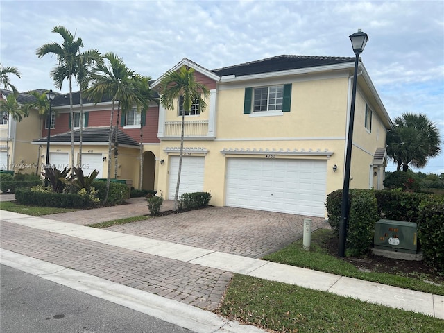 multi unit property featuring an attached garage, decorative driveway, and stucco siding