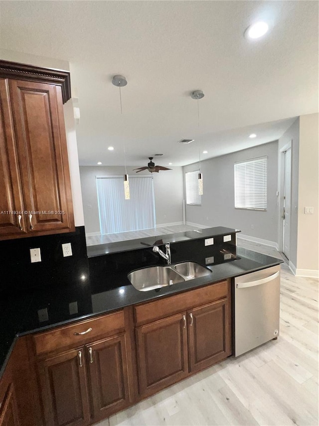 kitchen featuring stainless steel dishwasher, dark countertops, a sink, and decorative light fixtures