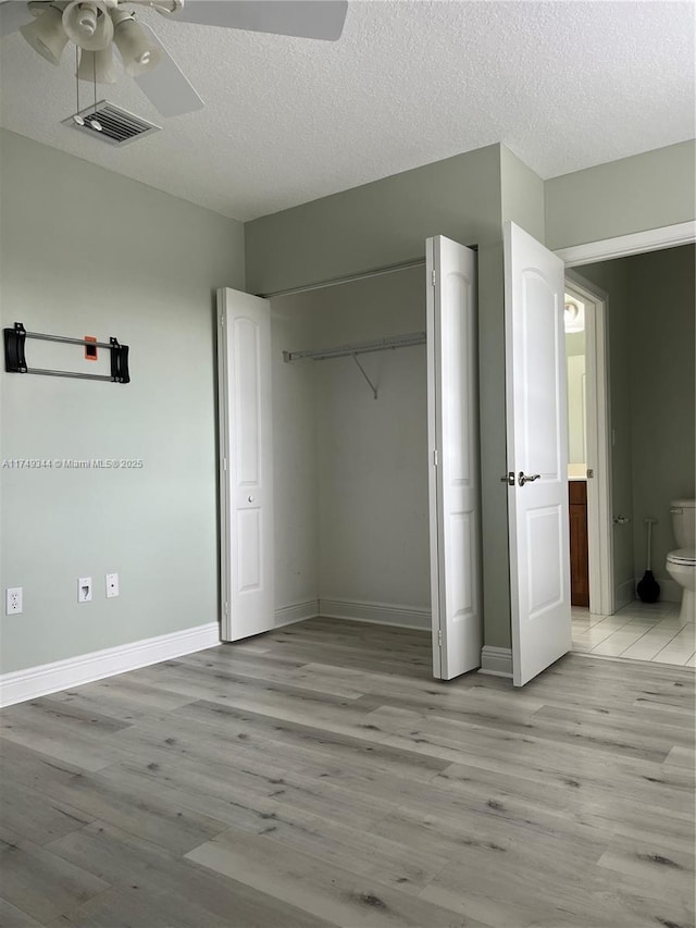 unfurnished bedroom featuring a closet, visible vents, a textured ceiling, and light wood finished floors